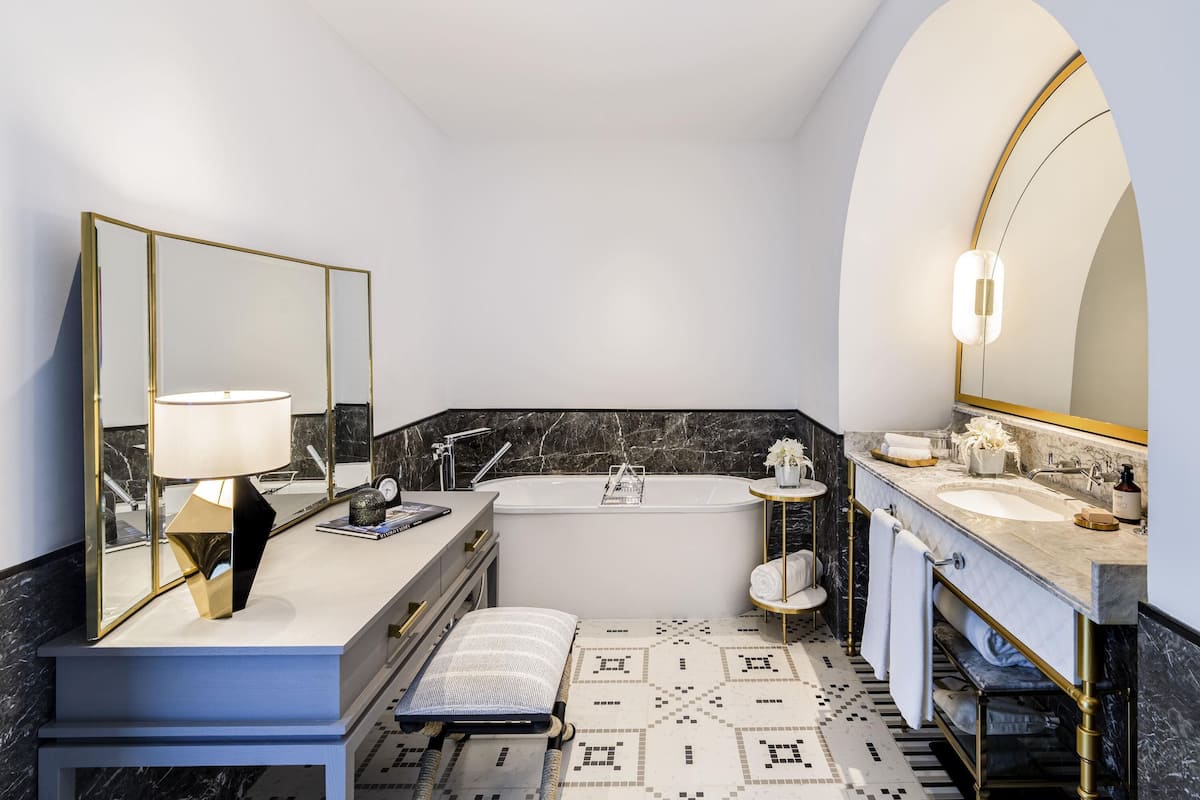 A modern bathroom with a large bathtub, a vanity with a mirror, and a bench.