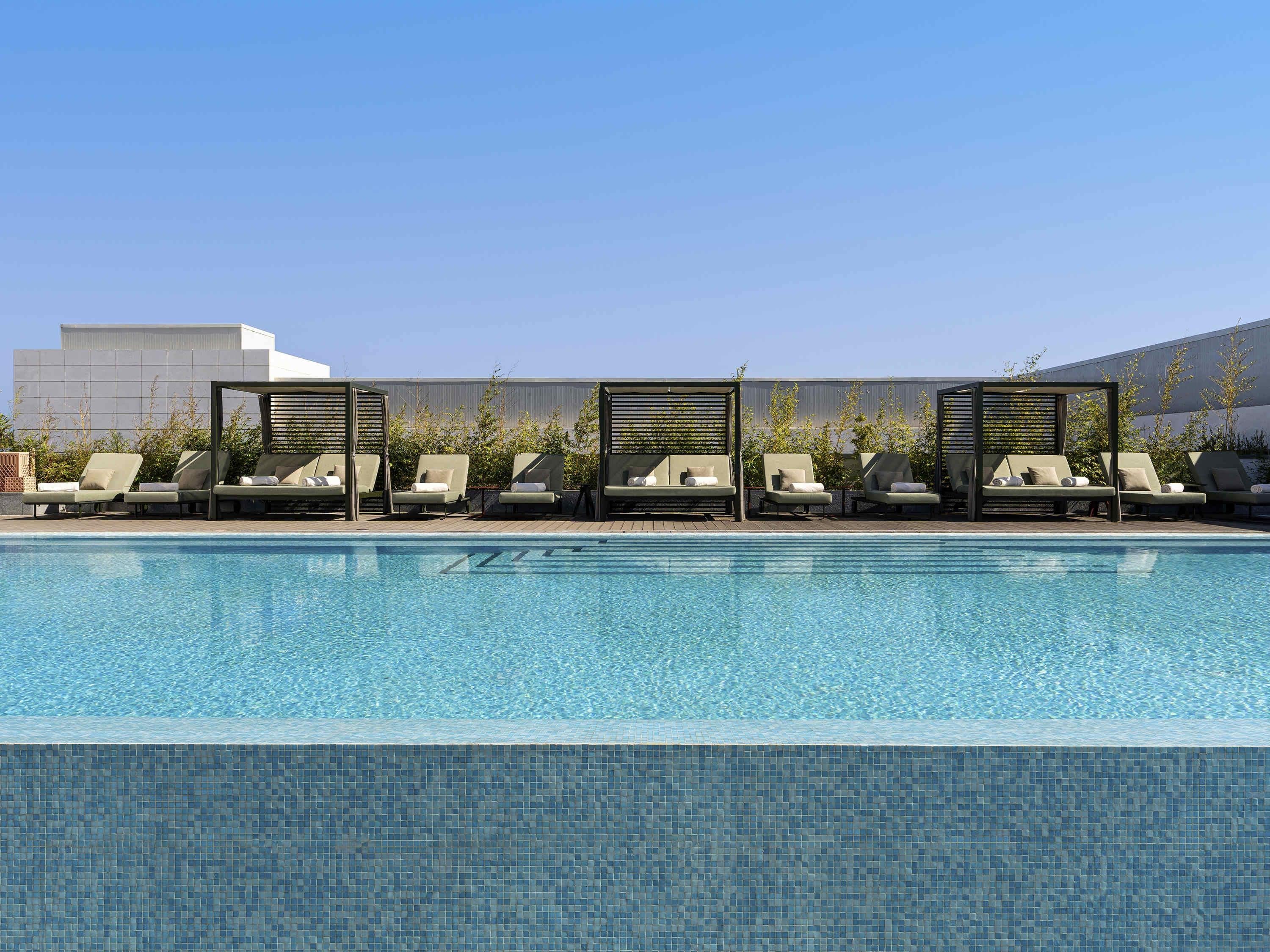 Una piscina con sillones de descanso y un edificio moderno al fondo.