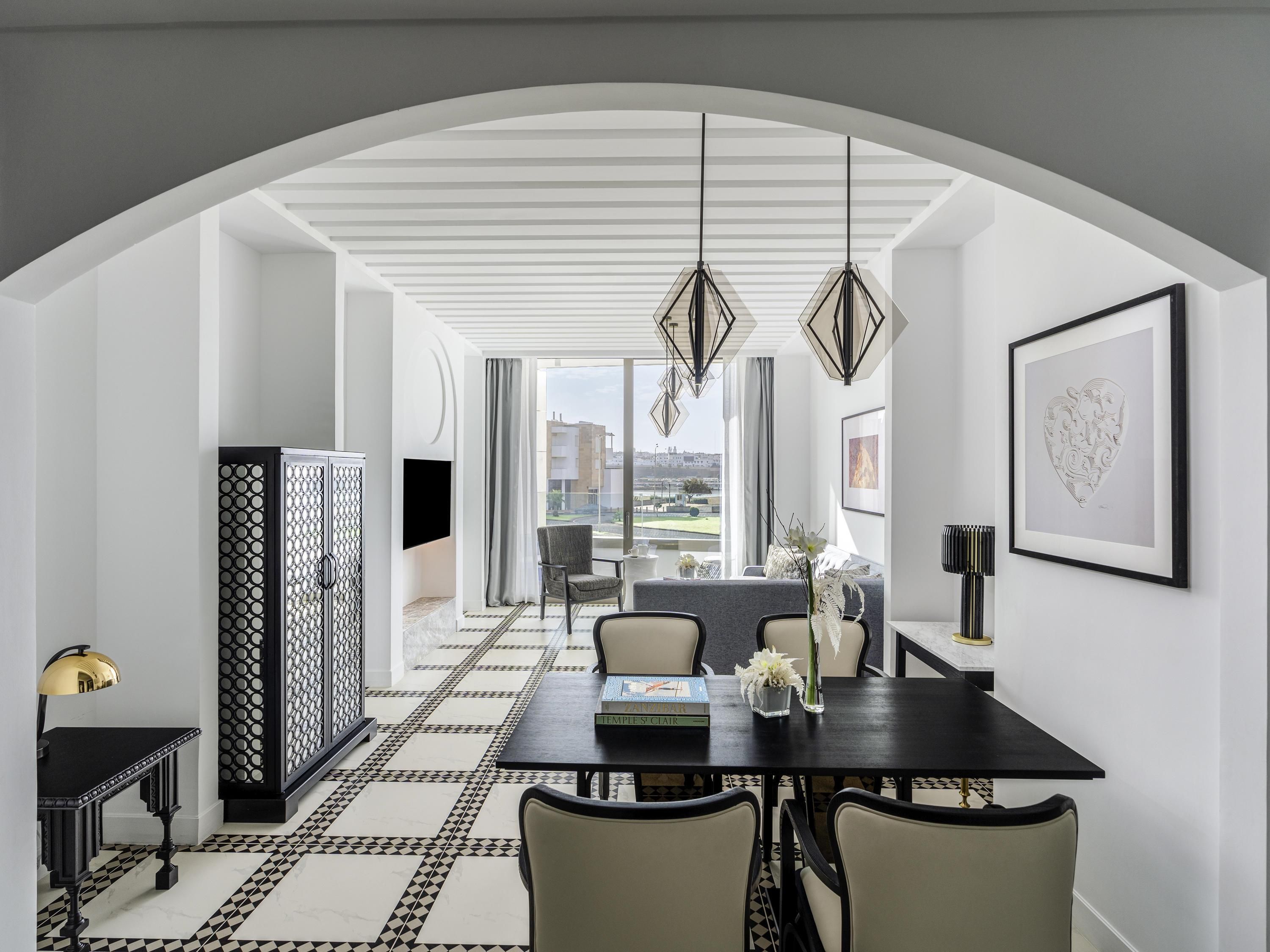 A dining area with a black table, white chairs, a patterned floor, and a view through an arched doorway.