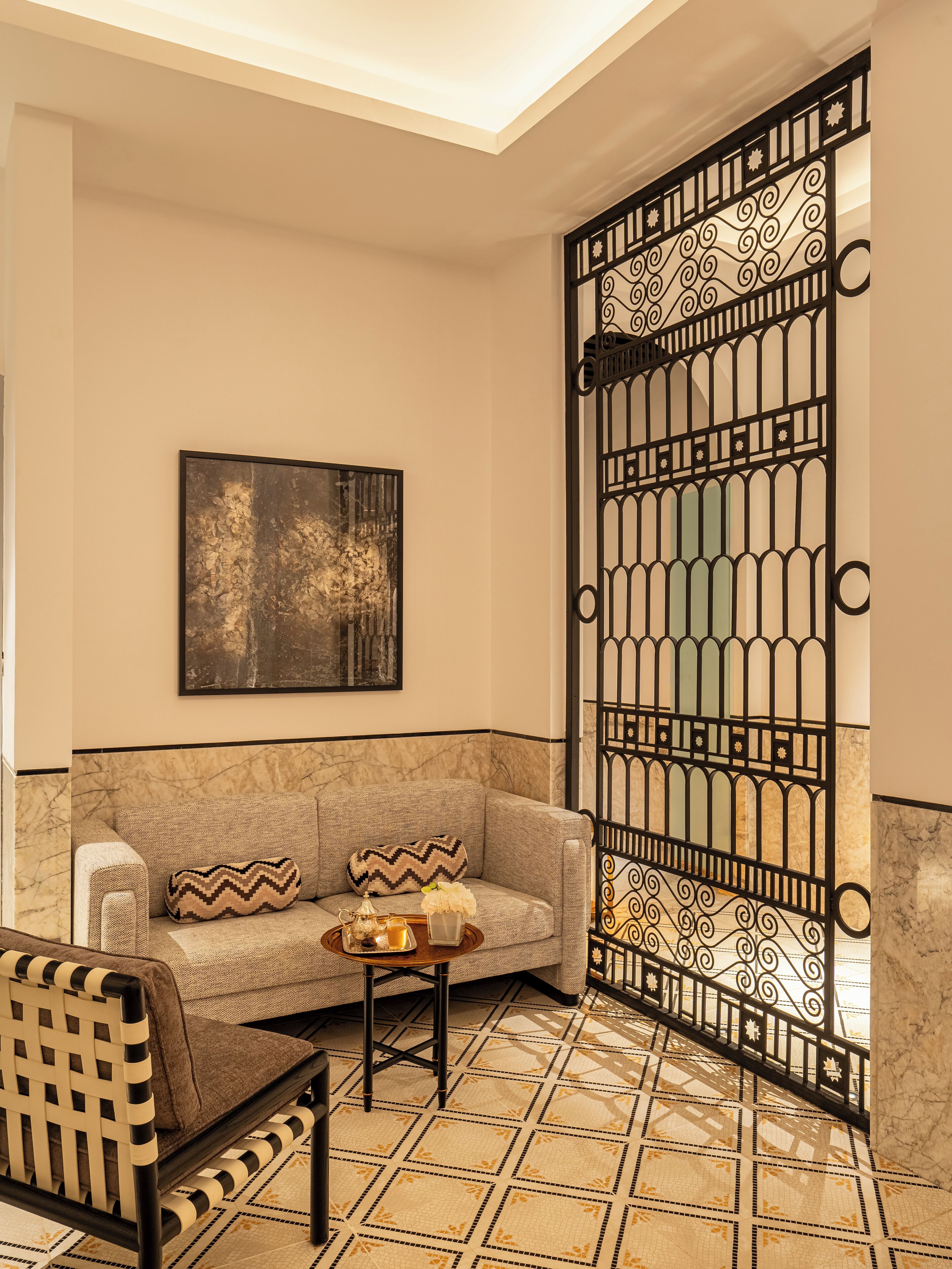 Quarto de canto com sofá, poltrona, grade decorativa, pintura e piso estampado.