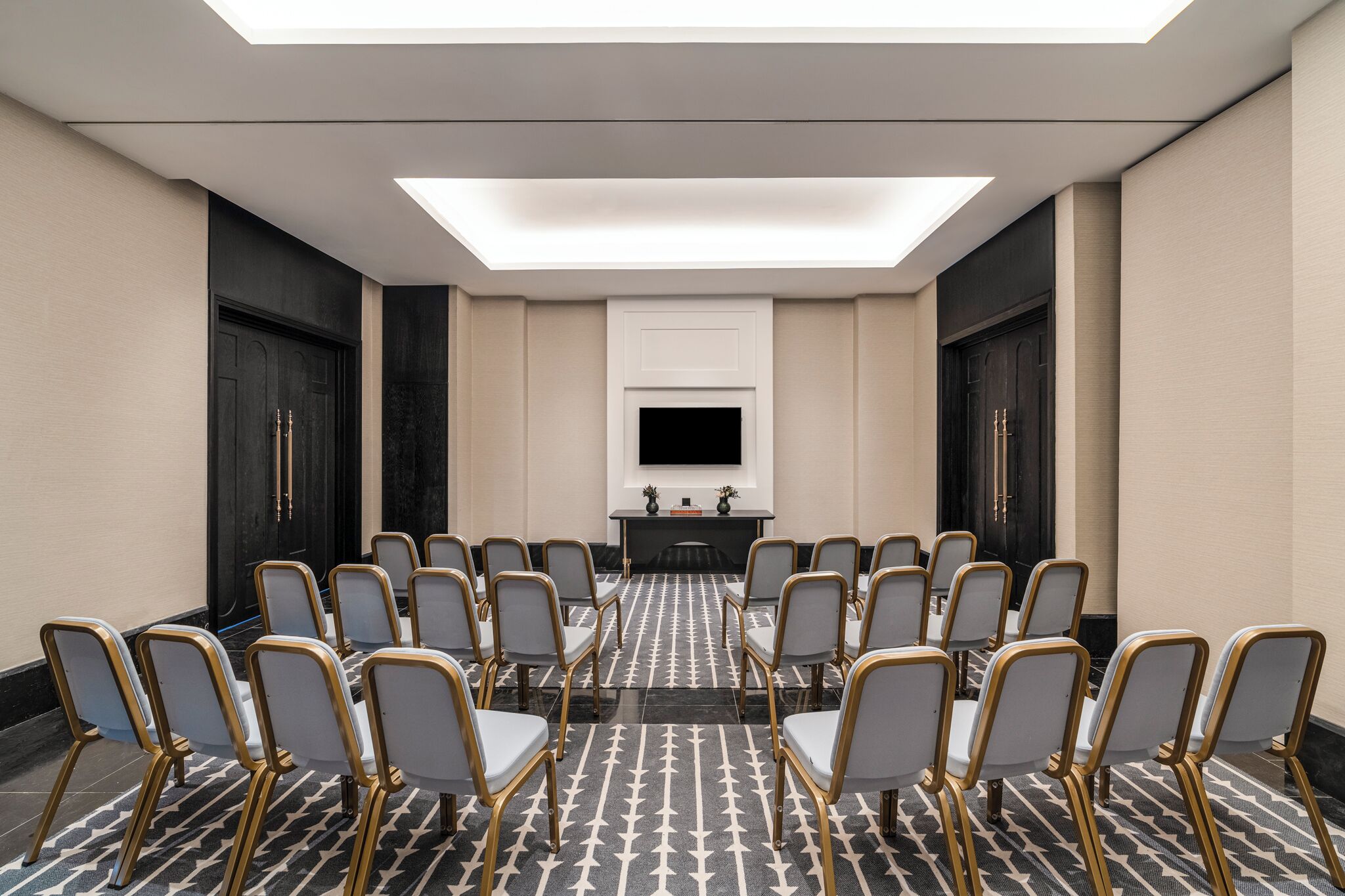 A conference room with a long table, rows of chairs, a flat-screen TV, and a patterned carpet.