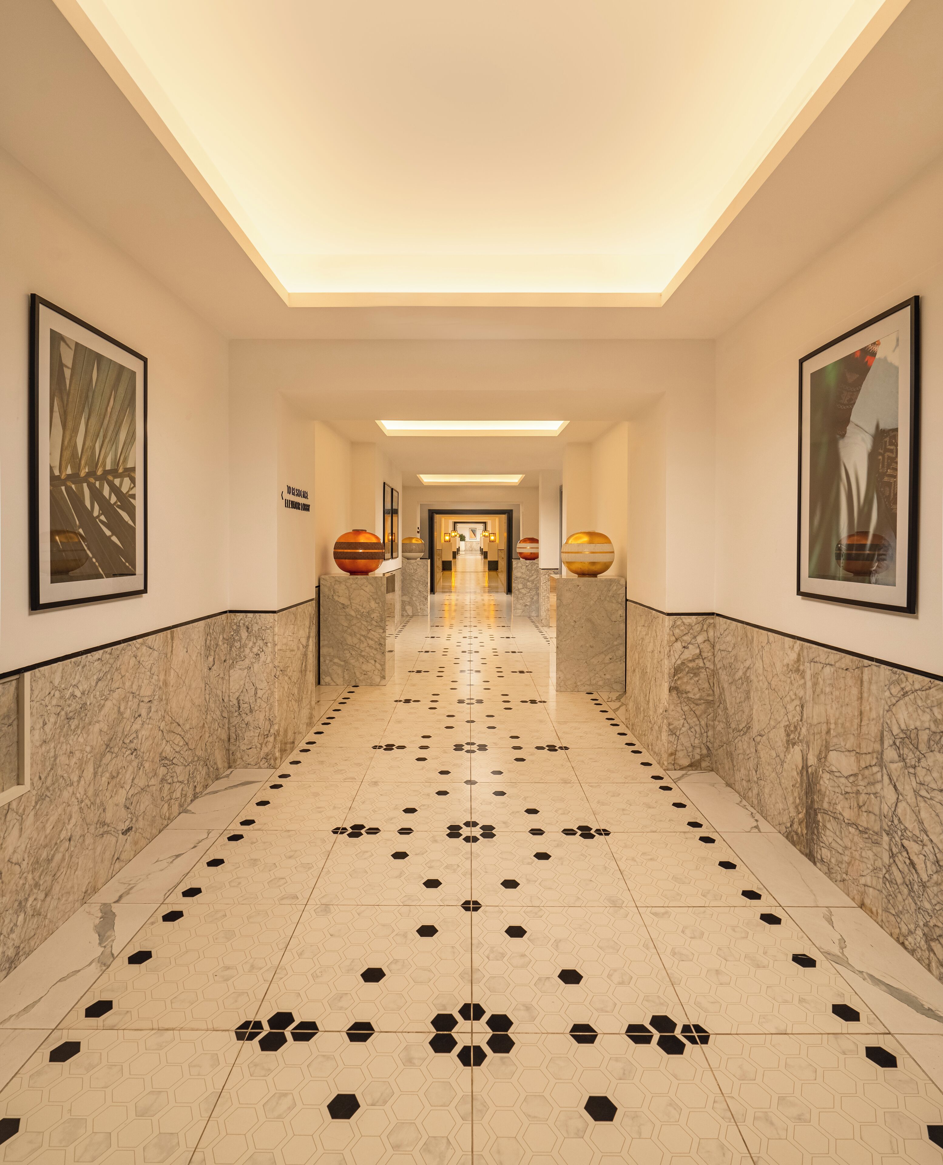 A hallway with marble walls, hexagonal patterned floor, and framed artwork.