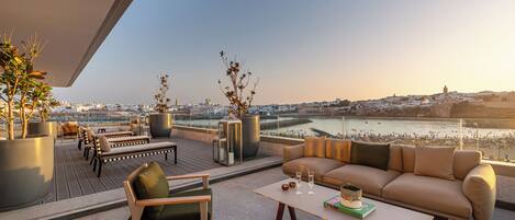 A rooftop terrace with seating, potted plants, and a view of a cityscape and river.