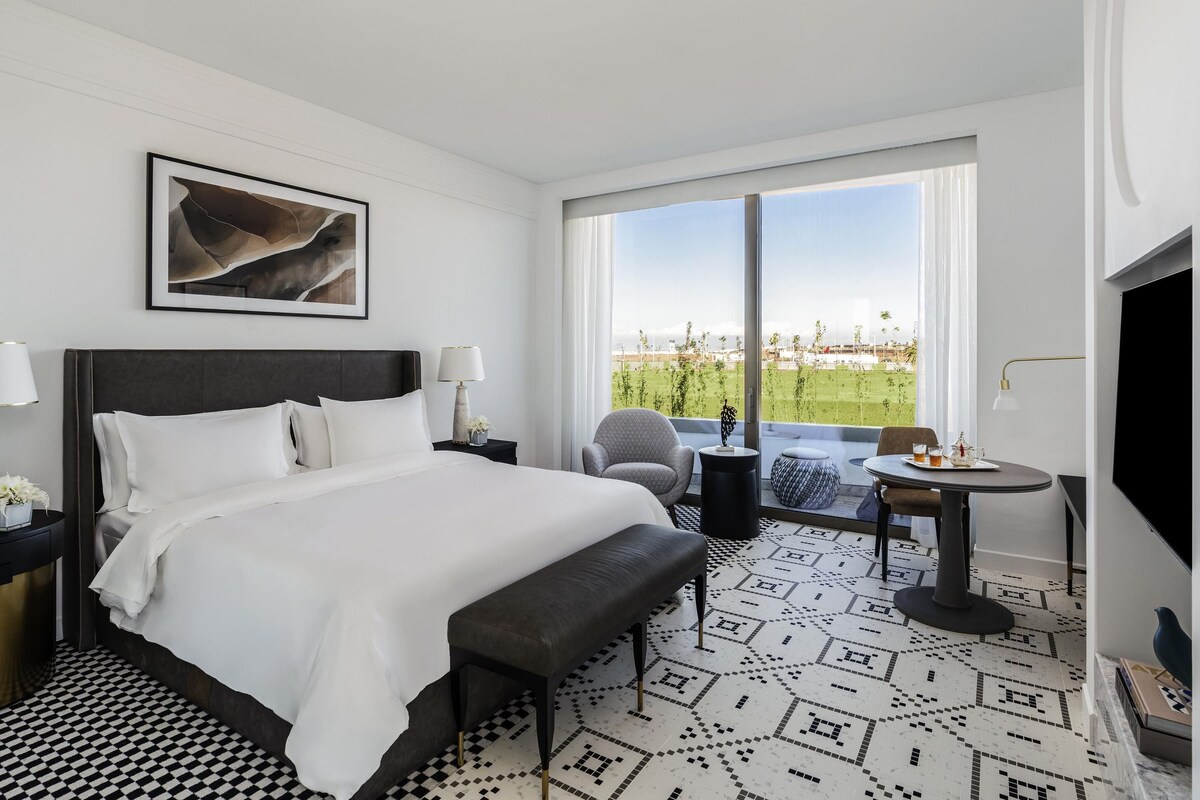 A hotel room with a large bed, a desk, a chair, and a TV.