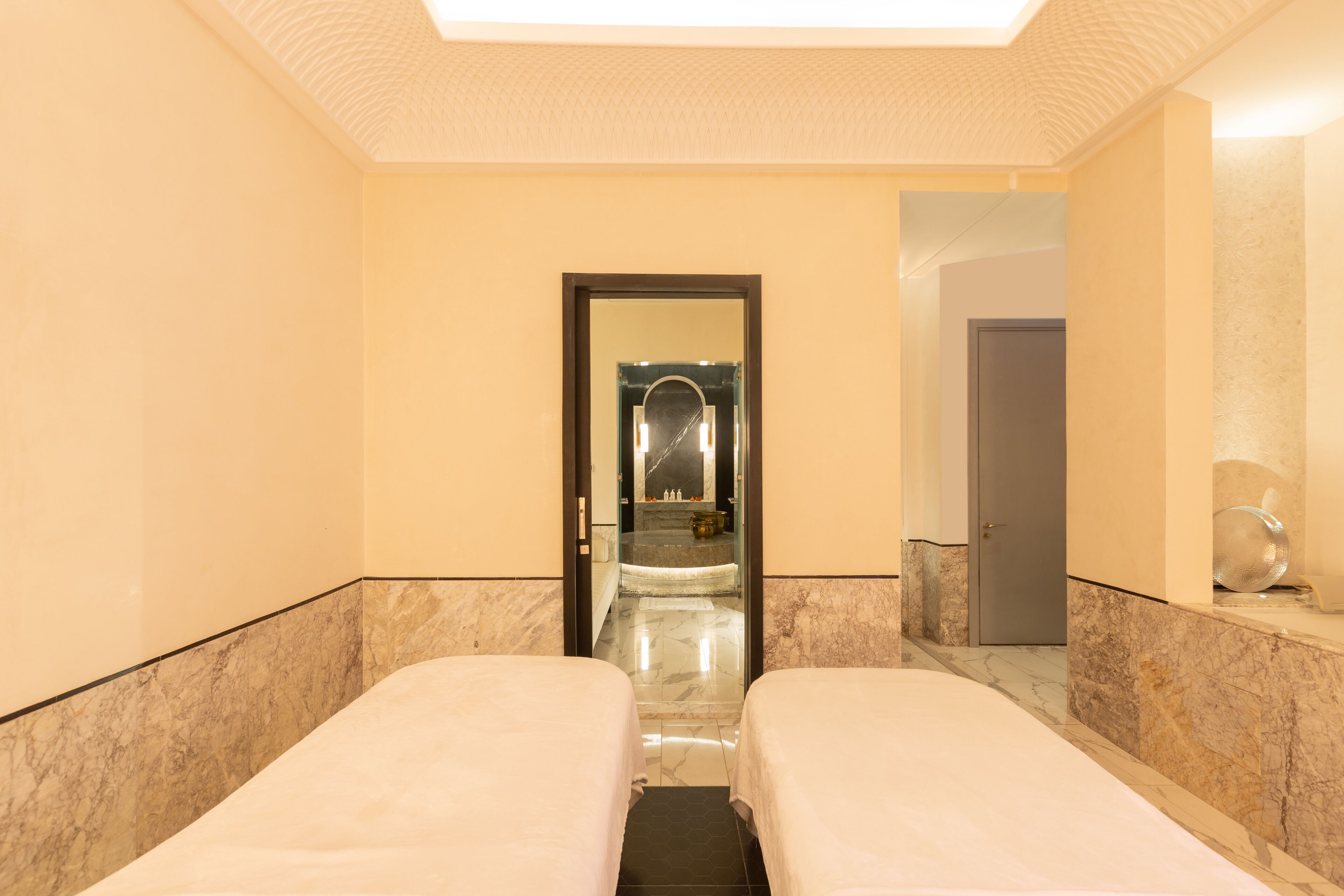 A hotel room with two single beds, a marble floor, and a large mirror on the wall.