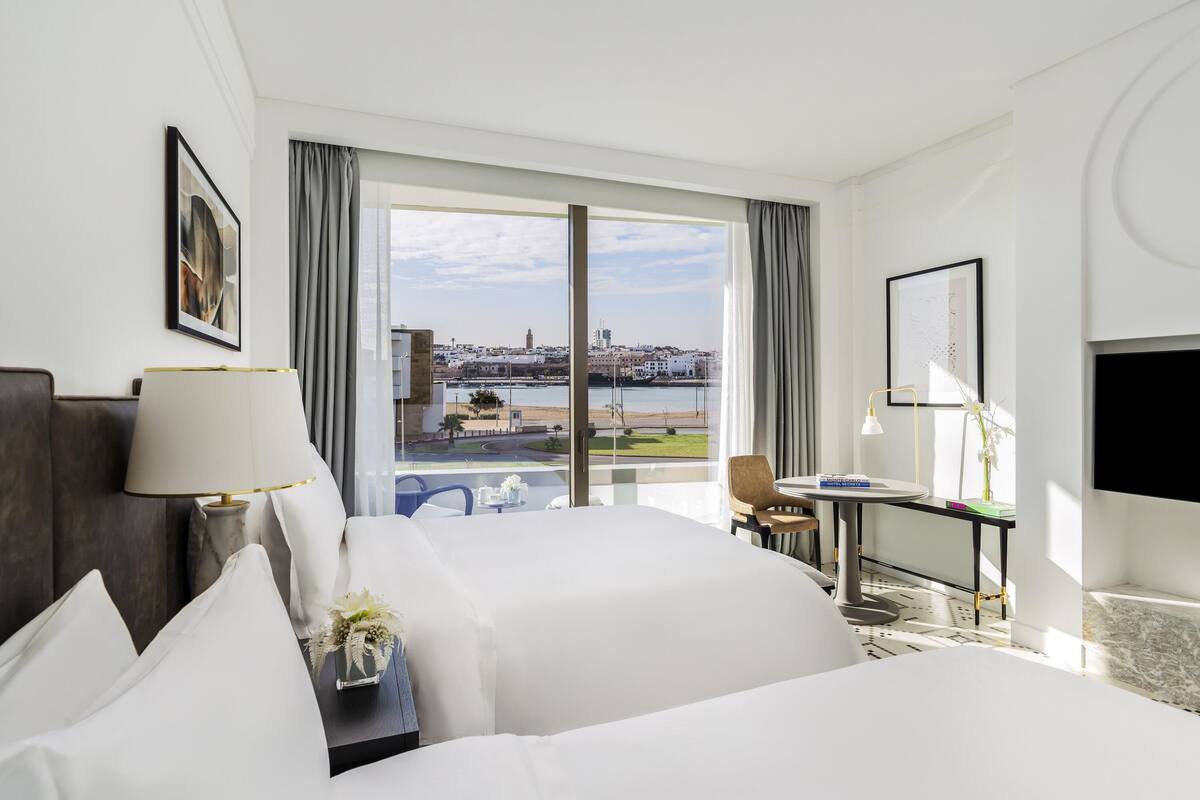 A hotel room with a large bed, a desk, a chair, a TV, and a view of the city and water.