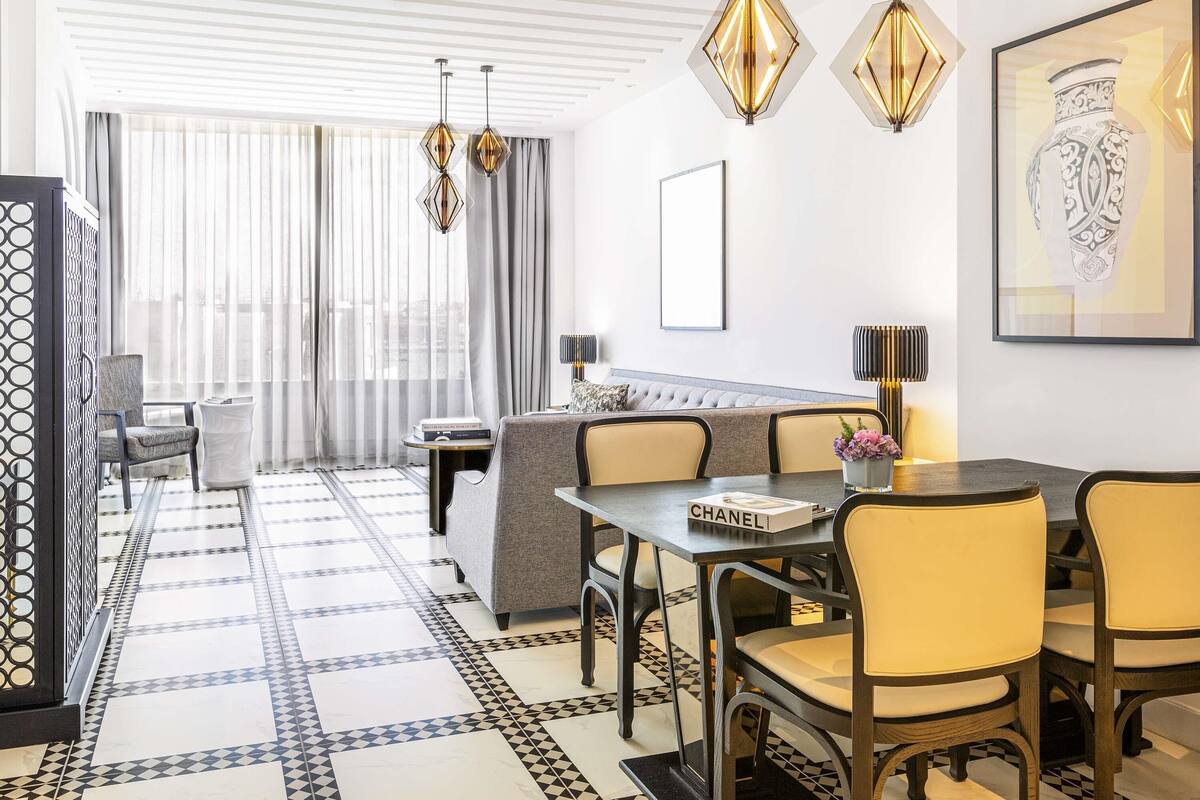 A modern hotel room with a dining area, a sofa, a table with a book, and a vase with flowers.