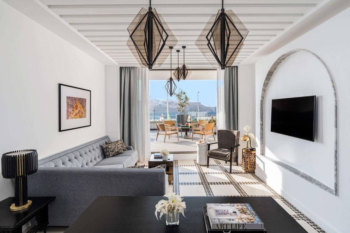 A modern living room with a sofa, a coffee table with a magazine, a TV mounted on the wall, and a view of the outside.