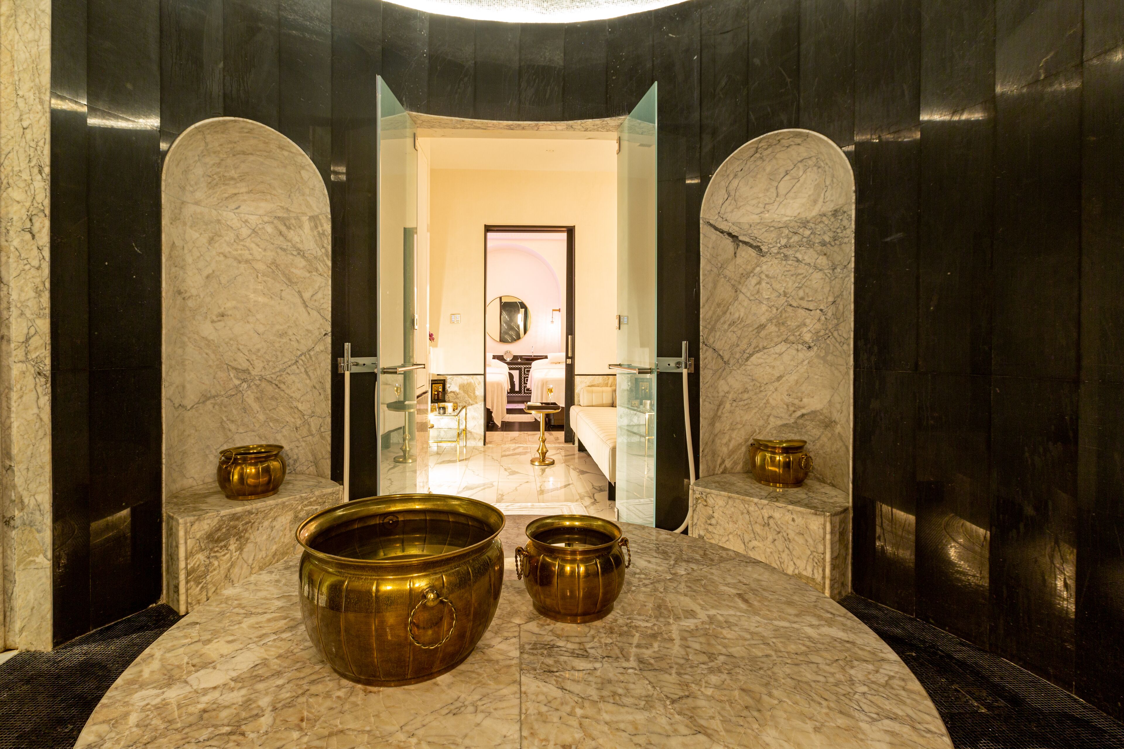 A luxurious bathroom with marble floors, two large brass basins, and a mirror above the sink.