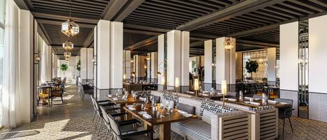 A spacious restaurant with high ceilings, modern chandeliers, and a patterned floor.