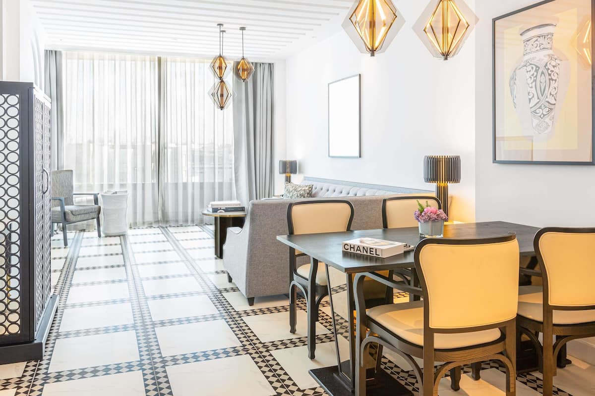 Moderni hotellihuone, jossa on ruokailutila, sohva ja suuri ikkuna, jossa on lÀpikuultavat verhot.