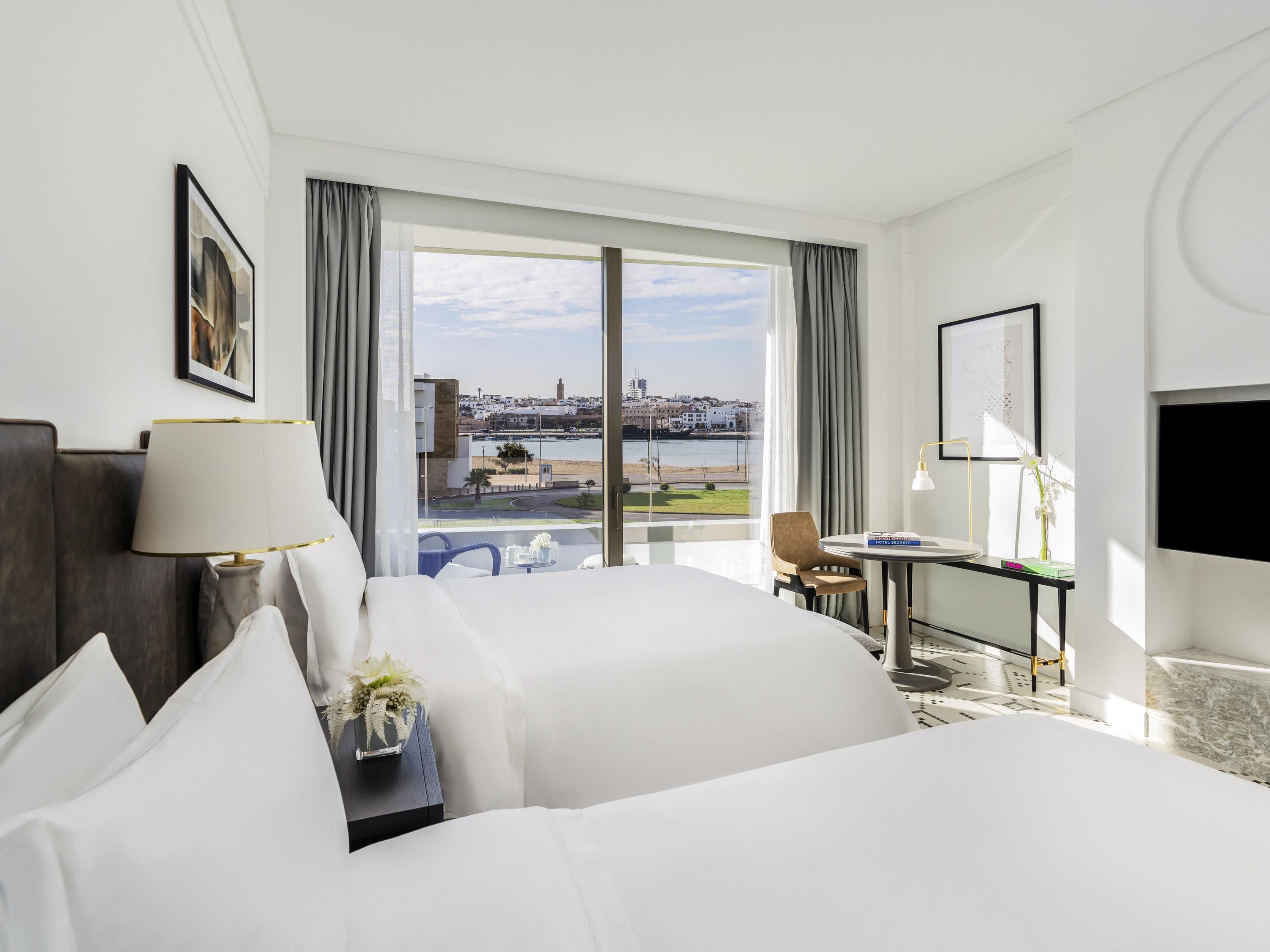 Habitación de hotel con una cama grande, un escritorio, una silla, un televisor y vistas a la ciudad y al agua.