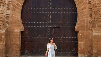 A woman walking in front of a large, ornate stone archway with a heavy wooden door.