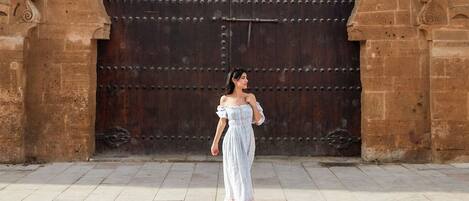 A woman walking in front of a large, ornate stone archway with a heavy wooden door.