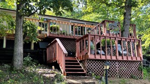 Une terrasse en bois avec un escalier menant à une zone abritée, le tout entouré d’arbres.