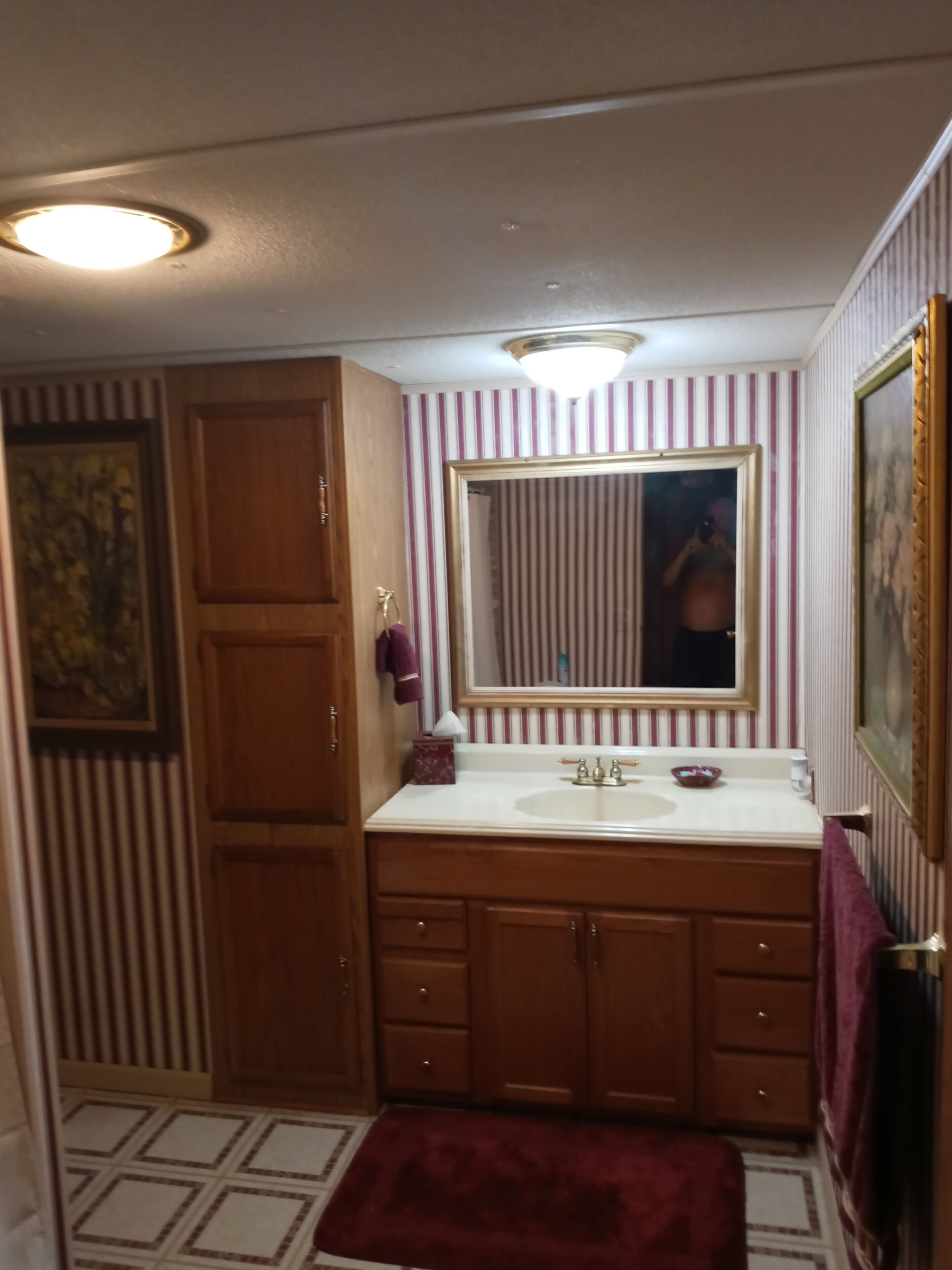A bathroom with a wooden vanity, a large mirror, striped wallpaper, and a red rug.