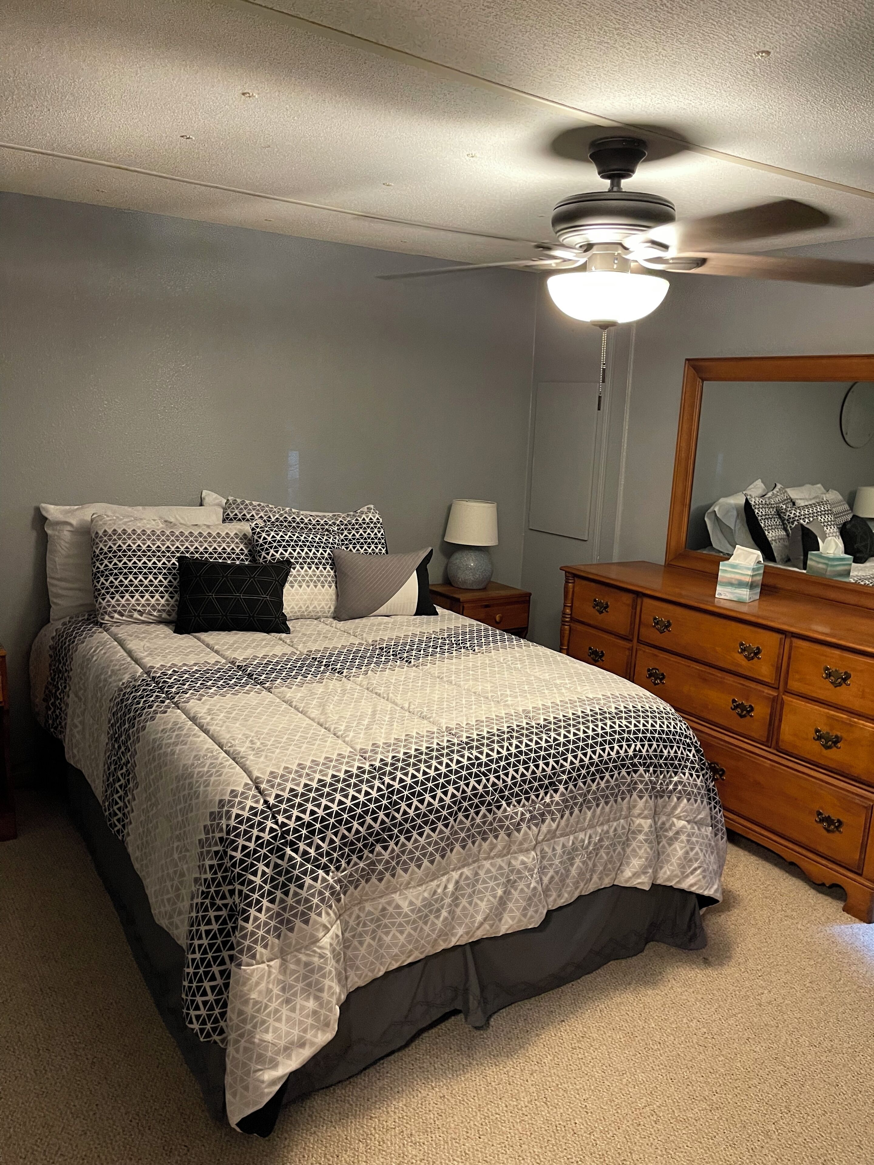 A bedroom with a bed, a nightstand, a dresser, a ceiling fan, and a mirror.