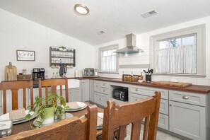 A modern kitchen with a wooden dining table, grey cabinets, a built-in microwave, and a window with curtains.