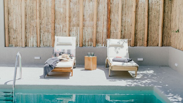 A poolside area with two lounge chairs, a small wooden stool, and a metal ladder leading into the pool. - Condo with private pool - 5 minutes from the beach (Pollonia)