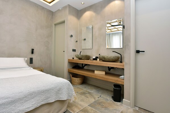 A modern bathroom with a large bed, two stone sinks, a mirror, and a wooden shelf. - Condominium with a private pool—5 minutes from the beach (Pollonia)