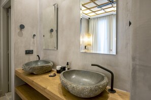 Een badkamer met twee grote stenen wastafels, een houten wastafelmeubel, een spiegel en een plafondlamp.