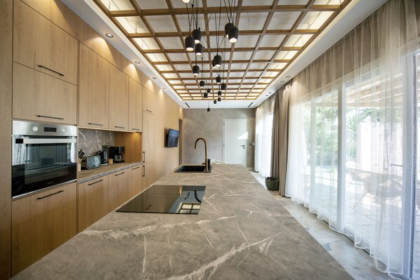 A modern kitchen with wooden cabinets, a built-in oven, and a large island with a glass top.