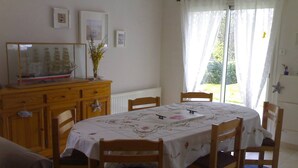 A dining area with a table set for four, wooden chairs, a wooden cabinet with a ship model, and a window with curtains. - Everything on foot and in the peace and quiet! (Pléneuf-Val-André)