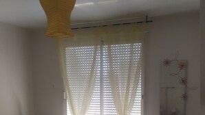 A bedroom with a bed, two chairs, a small table, a TV, and a window with sheer curtains. - Everything on foot and in the peace and quiet! (Pléneuf-Val-André)