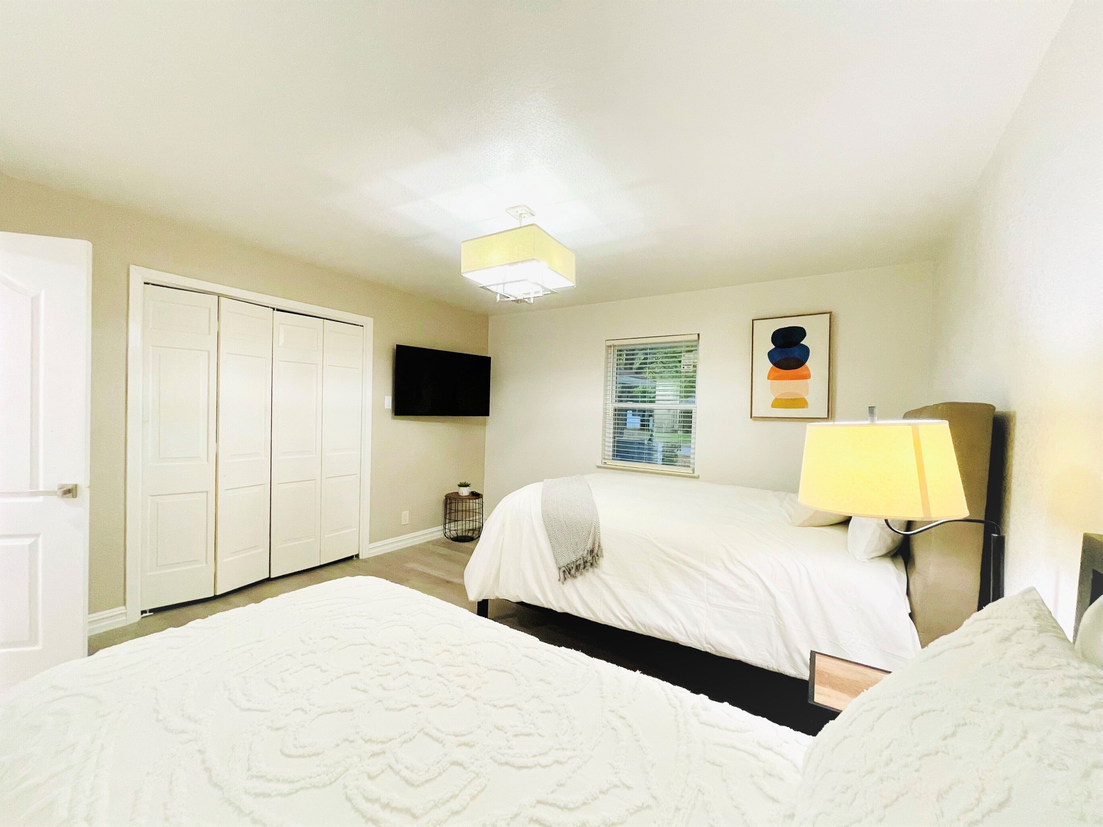 Une chambre à coucher avec un lit, une table de chevet avec une lampe, un téléviseur fixé au mur et une armoire.