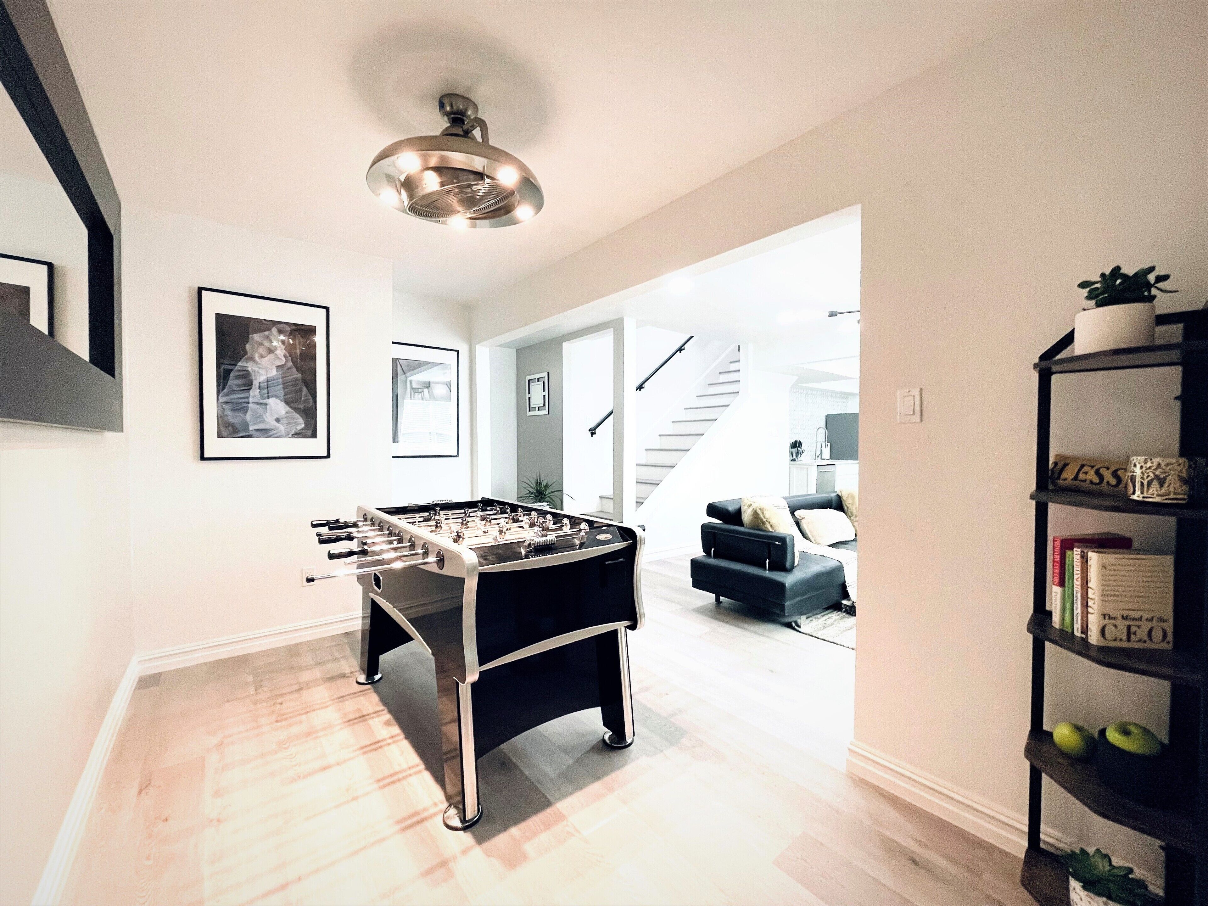 Una sala de estar moderna con mesa de fútbol, una estantería y una escalera que sube a otro nivel.