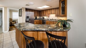 A kitchen with wooden cabinets, a granite countertop, and two black chairs.