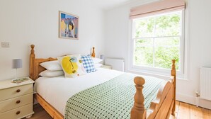 A bedroom with a wooden bed, white walls, a window with a view of greenery, a bedside table with a lamp, and a framed picture on the wall. - Large family home in Sandwich - Poplar House (Sandwich)