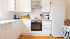 A compact kitchen with white cabinets, a Bosch oven, a Bosch refrigerator, and a wooden chair. - Large family home in Sandwich - Poplar House (Sandwich)