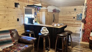 Un acogedor interior de cabaña con una zona de bar de madera, un sofá de cuero y una manta estampada.