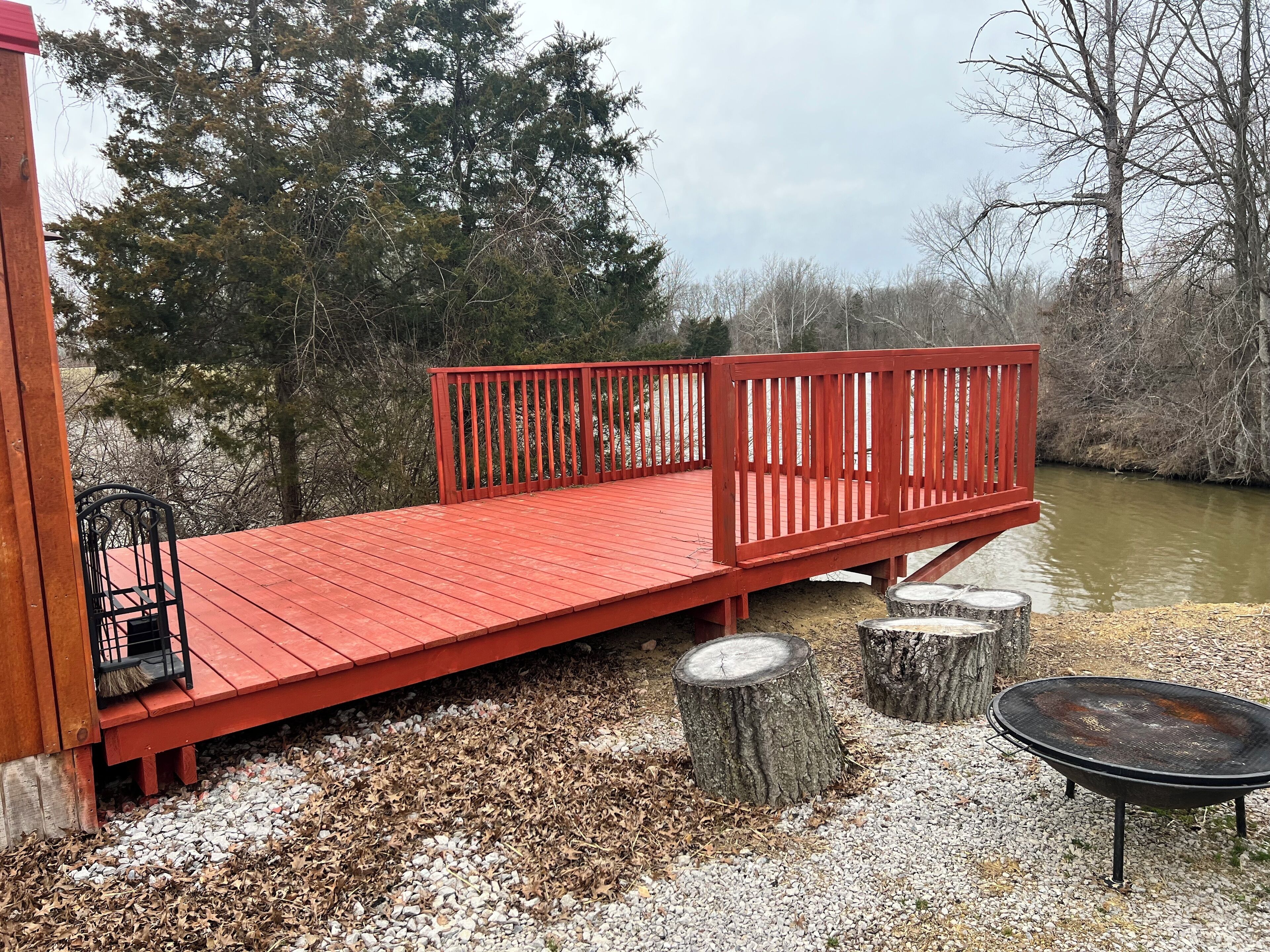 A red wooden deck with a metal bench and a fire pit.
