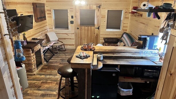 Interior acogedor de una cabaña de madera, con zona de comedor, taburete de bar y pequeña cocina.