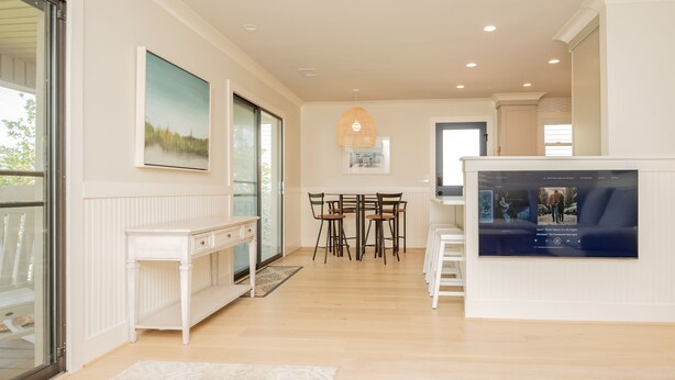 A spacious living area with a white console table, a dining table with chairs, a large TV screen, and a painting on the wall. - Wingspan: Modern, Elegant Home Close to the Intracoastal Waterway (Oak Island)