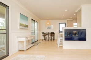 A spacious living area with a white console table, a dining table with chairs, a large TV screen, and a painting on the wall.
