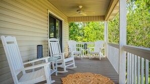A covered porch with white rocking chairs and a glass table, surrounded by greenery. - Wingspan: Modern, Elegant Home Close to the Intracoastal Waterway (Oak Island)