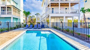A swimming pool with lounge chairs and a fenced area, surrounded by buildings with balconies and a clear sky. - Gulfview new construction w/private, heated pool and beach gear! (Port St Joe)