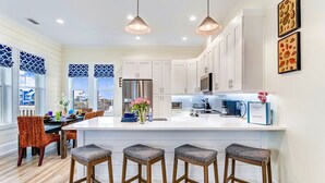 A modern kitchen with white cabinets, a large island with bar stools, pendant lighting, and a view of the outside. - Gulfview new construction w/private, heated pool and beach gear! (Port St Joe)