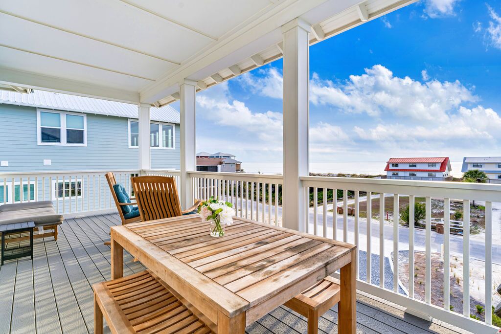 A wooden deck with a table and chairs, a white railing, and a view of buildings and a clear sky.