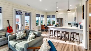 A spacious living area with a sofa and a dining table, a kitchen with white cabinets and a bar area, and large windows with patterned valances. - Gulfview new construction w/private, heated pool and beach gear! (Port St Joe)