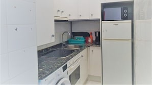 Une cuisine compacte avec des meubles blancs, un évier à deux bacs, un four à micro-ondes, une machine à café et un lave-linge.