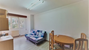 Une pièce de taille modeste comprenant un canapé, une table à manger avec des chaises, un petit bureau et un radiateur.