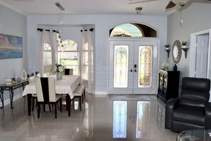 A spacious living area with a dining table, chairs, a black leather sofa, and a glass coffee table.