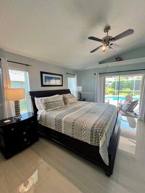A bedroom with a bed, nightstands, a ceiling fan, and a view of a pool outside. - Gorgeous Private Retreat-Port St Lucie Pool (Port St. Lucie)