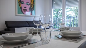 A dining table set with white plates, glasses, and cutlery, with a black sofa and a window in the background. - Vat 52 Sub 15 - One Bedroom Apartment, Maximum 4 Guests (Udine)