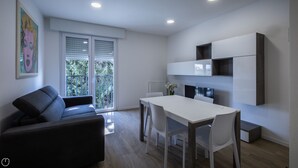A modern living room with a sofa, a dining table with chairs, and a kitchen area with cabinets. - Vat 52 Sub 15 - One Bedroom Apartment, Maximum 4 Guests (Udine)