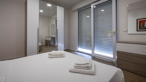 A modern hotel room with a large bed, a mirror, a sliding glass door with blinds, and a framed picture on the wall. - Vat 52 Sub 15 - One Bedroom Apartment, Maximum 4 Guests (Udine)